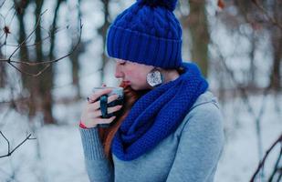 Portrait of young red hair girl with freckles wearing at blue knitted wool hat and scarf with cup of tea in winter day. photo