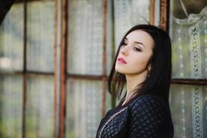 Brunette model girl at leather jacket posed background old wooden house with windows. photo