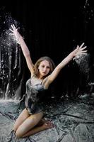 Girl dancer jumping and dancing in the white dust with flour on a black background. Studio shot of woman dancing with flour. photo