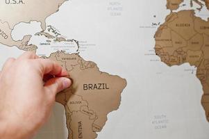 Scratch travel map of the world. Hand of man erase Brazil with coin. photo