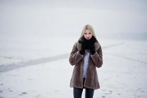 retrato de joven elegancia chica rubia en un abrigo de pieles río niebla de fondo en el hielo de invierno. foto