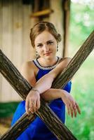 joven con sobrepeso en vestido azul plantea jardín de primavera de fondo en cabaña de madera. foto