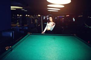 Young curly girl posed near billiard table. Sexy model at black mini mini skirt play russian snooker. Play game and fun concept. photo