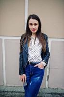 Portrait of stylish young girl wear on leather jacket and ripped jeans with mobile phone at hand. Street fashion model style. photo