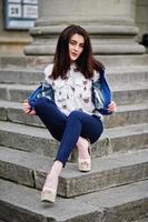 Young stylish brunette girl on shirt, pants, jeans jacket and high heels shoes, posed at stone stairs. Street fashion model concept. photo