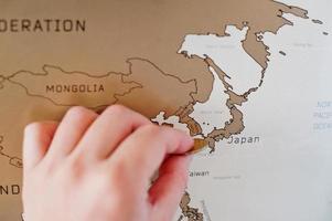 Scratch travel map of the world. Hand of man erase Japan with coin. photo