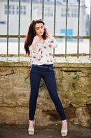 Young stylish brunette girl on shirt, pants and high heels shoes, posed background iron fence. Street fashion model concept. photo