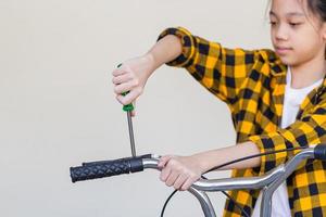 niña reparando su bicicleta en el garaje, niña usando un destornillador arreglando bicicletas, pasatiempos y conceptos de reparación foto