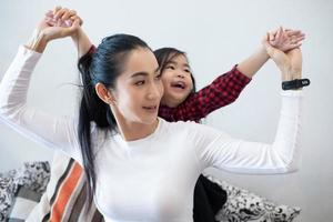 The daughter is hugging and playing with her mother and laughing and smile happy on the sofa while relaxing at home. photo