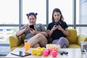 mujer asiática con sobrepeso con un amigo juega al teléfono móvil y disfruta comiendo en el sofá de casa