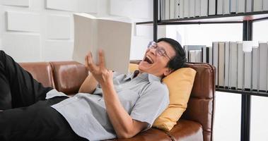 Senior Asian man reading book on sofa in living room at home ,Portrait of Asian elderly man is Relaxing and Happiness With Read a Magazine  at home photo