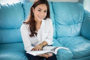 Asian women smiling and reading a book for relaxation on sofa at  home photo