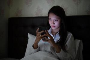 Asian woman using a mobile phone on night at the bed.She smiles and enjoys at home. photo