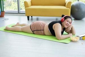 mujer asiática usando tableta y. usando auriculares para escuchar música y ella está haciendo ejercicio en casa, una chica asiática disfruta comiendo comida foto