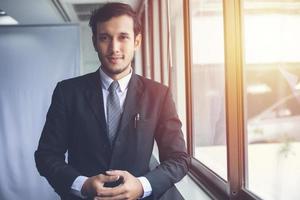 Happy handsome businessman standing and smiling in office photo