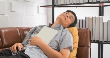 Senior Asian man reading book and sleep on sofa in living room at home ,Portrait of Asian elderly man is Relaxing and Happiness With Read a Magazine photo