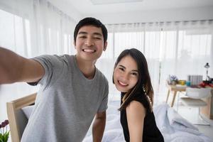 Asian couple lovers lying on their play mobile phones and selfie on bed  at home photo