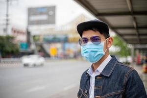 Asian Young man standing in the city and wearing protection mask on face for protection air pollution, particulates and for protection flu virus, influenza, coronavirus at city photo