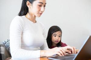 las madres asiáticas están enseñando a sus hijas a leer un libro y a usar cuadernos y tecnología para el aprendizaje en línea durante las vacaciones escolares en casa. conceptos educativos y actividades de la familia foto