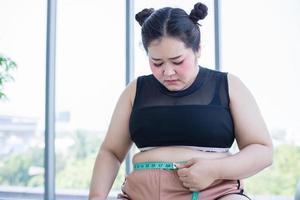 Asian overweight woman measuring fat layer with waistline at home photo