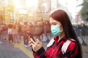 mujer joven asiática que usa un teléfono inteligente en la ciudad con mascarilla debido a la contaminación del aire, partículas y para protegerse del virus de la gripe, la influenza, el coronavirus foto