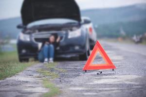 mujer asiática sentada en el suelo cerca de un camión averiado con un triángulo rojo de un camión en la carretera foto