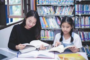 dos estudiantes asiáticas leyendo libros y usando un cuaderno en la biblioteca.