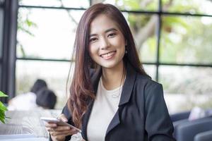 mujeres de negocios asiáticas que usan portátiles y teléfonos inteligentes y mujeres de negocios que sonríen felices por trabajar foto