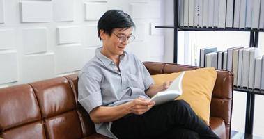un anciano asiático leyendo un libro en el sofá de la sala de estar en casa, el retrato de un anciano asiático se relaja y se siente feliz leyendo una revista en casa foto