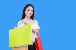 Beautiful asian young woman is standing holding shopping bags .She smile happiness in the shopping mall on blue background photo