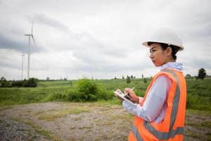 Asian engineer with hardhat using  tablet pc computer inspecting and working at wind turbine farm Power Generator Station photo