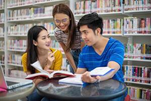 los estudiantes asiáticos del grupo sonríen y leen libros y usan un cuaderno para ayudar a compartir ideas en el trabajo y el proyecto. y también repasar el libro antes del examen foto