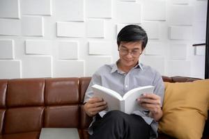 un anciano asiático leyendo un libro en el sofá de la sala de estar en casa, el retrato de un anciano asiático es relajante y feliz con leer una revista foto