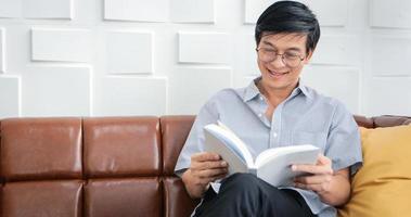 un anciano asiático leyendo un libro en el sofá de la sala de estar en casa, el retrato de un anciano asiático se relaja y se siente feliz leyendo una revista en casa foto