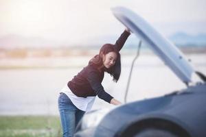 mujer asiática revisando un auto averiado en la calle foto