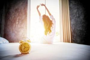 despertador teniendo un buen día de mujer asiática despertándose en su cama completamente descansada y abriendo las cortinas por la mañana para tomar aire fresco en casa foto