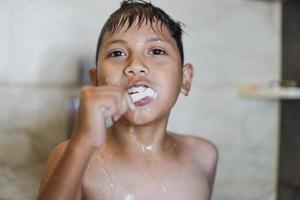 niño asiático cepillando los dientes con espuma saliendo de su boca foto