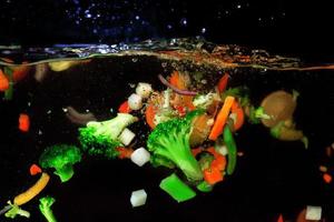 paprika, carrot, broccoli, onion falling in the boiling water on dark background. Underwater view. Cooking, vegetarian, cooking at home concept photo