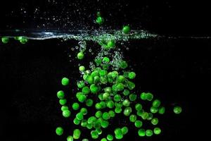guisantes verdes cayendo en el agua hirviendo sobre fondo oscuro. vista submarina. concepto de cocina, vegetariano, cocina en casa foto