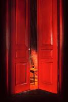 empty chair in light behind red massive vintage doors indoor. Old fashioned interior concept photo