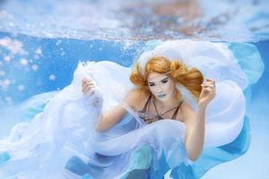 retrato de moda bajo el agua de una hermosa joven rubia con vestido azul foto