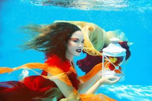 Underwater fashion portrait of beautiful blonde young woman in red dress with lamp photo