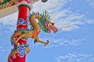majestuosa estatua de dragón chino asiático volador dorado con muro de hormigón rojo y cielo azul en un día soleado