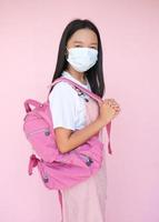 Student young girl wear mask with backpack on pink background. photo