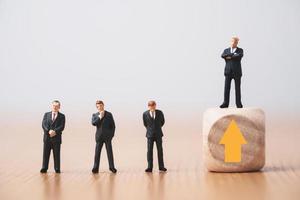 Businessman standing on wooden cube which higher level from three businessmen standing on floor for promotion from staff to management concept. photo