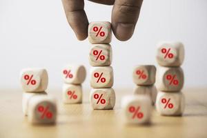 Hand holding and stacking red percentage sign print screen on wooden cube block for interest rate and business profit growth concept. photo