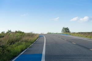 camino curvilíneo cuesta arriba de la carretera asfaltada con senderos laterales para bicicletas. bajo el cielo azul de fondo. foto