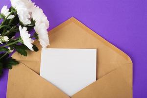 Opened craft paper envelope with empty piece of paper and white flowers near on very peri background photo