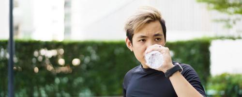 Active Asian sportsman relaxing and drinking a water in bottle after outdoor running or workout. Asian man drink a water during the break from exercise. A healthy man trying hard for cardio workout. photo