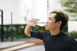 Active Asian sportsman relaxing and drinking a water in bottle after outdoor running or workout. Asian man drink a water during the break from exercise. A healthy man trying hard for cardio workout.